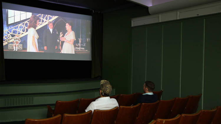 Two people sit in a small theatre watching a movie