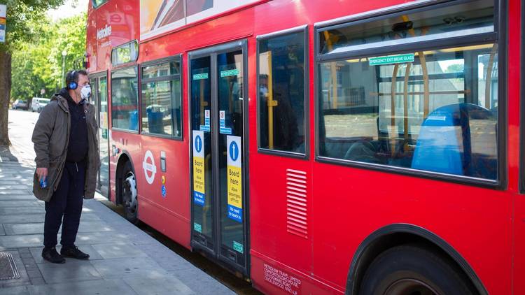 man with a mask waiting for a london bus 