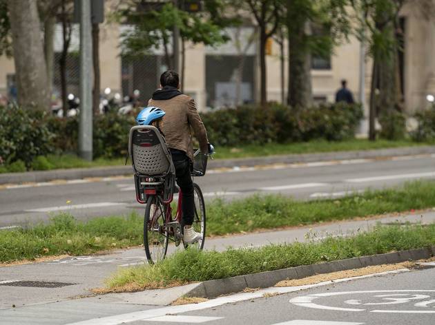 Un home circula pel carril bici amb el seu infant al seient de la bicicleta Un home circula pel carril bici amb el seu infant al seient de la bicicleta
