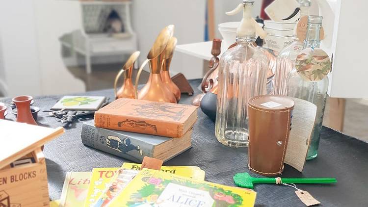 A table with items like books, a spoon, glass bottles and copper jugs on it