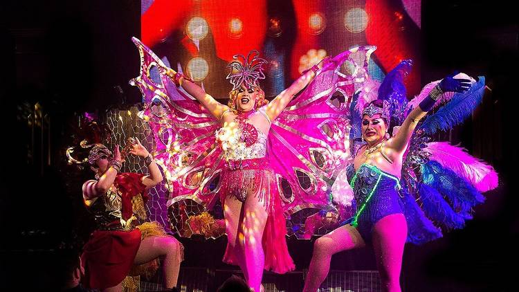 Three drag queens pose in extravagant costumes.