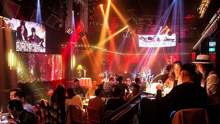 Image of venue with people sitting at tables, coloured lighting.