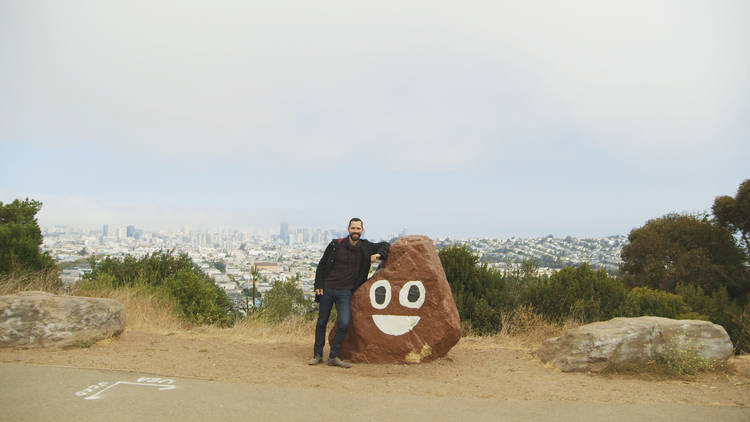 Man leaning on a rock painted like the poop emoji in Picture Character / C-Doc in the Clouds