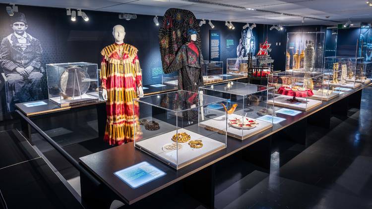 Interior of exhibit, ornate dresses at the centre surrounded by ritual objects.