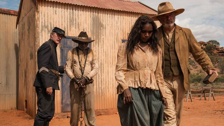 A still from Sweet Country featuring character Lizzie being led away by Fred Smith while Sam Kelly and Fletcher stand in the background