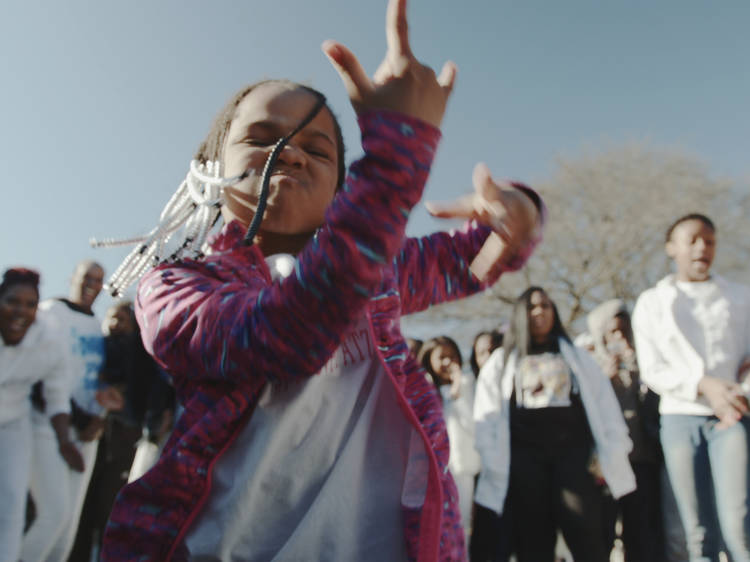 Still from Dark City Beneath the Beat featuring a small girl dancing in the centre of a crowd