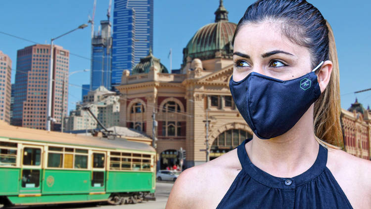 A close up of a woman wearing a black face mask; a tram and Flinders Street Station are in the background