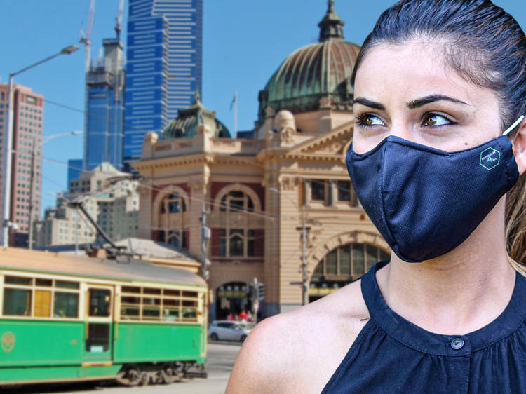 A close up of a woman wearing a black face mask; a tram and Flinders Street Station are in the background