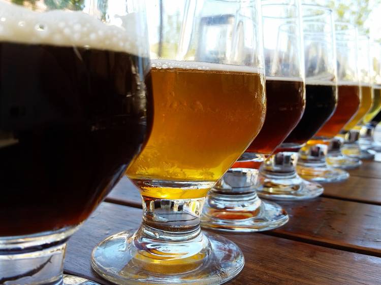 Line of beer glasses filled with different coloured beers on wooden table