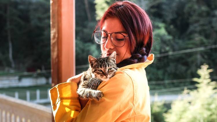 Woman in a yellow coat giving a cat a hug