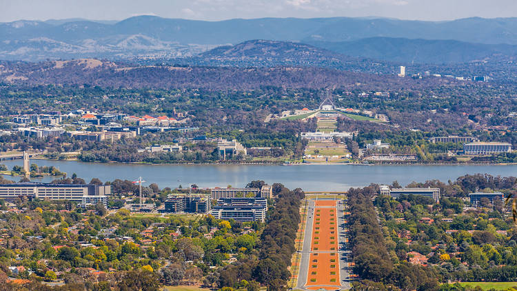 View of Canberra from Mount Ainslie lookout - ANZAC Parade, Parliament House and modern architecture with mountains in background. ACT, Australia