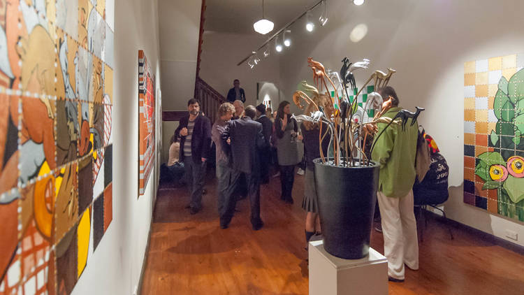 People standing around in a white, narrow gallery looking at various artworks