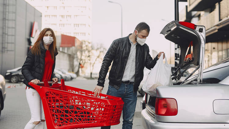 A man and a woman unloading groceries from a shopping trolley into a sedan car in a carpark