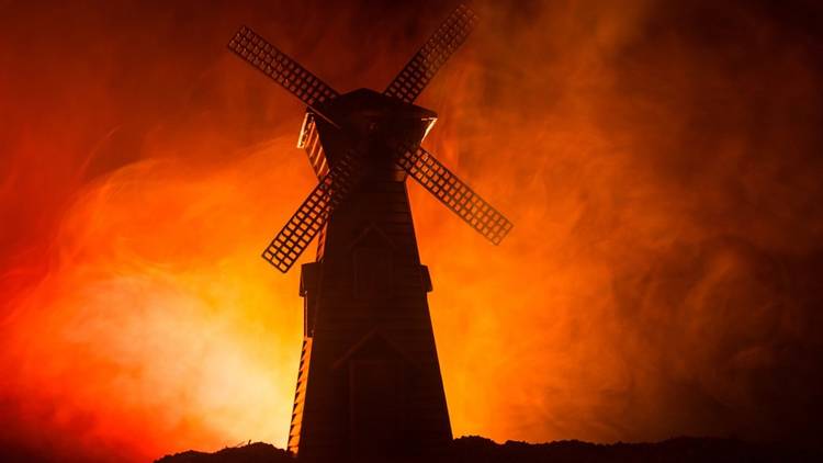 A windmill silhouetted by haze lit by fire