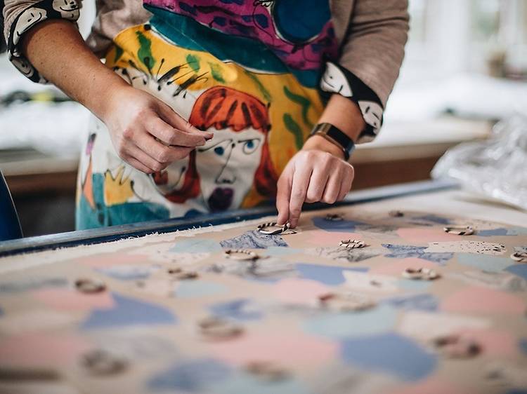 A person rearranges ceramic jewellery on a patterned blanket