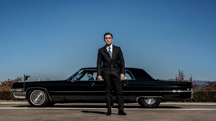 Man in a suit standing by a 1970s black limousine