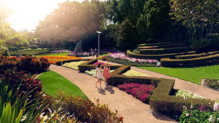 Two women in sundresses walking past flower gardens