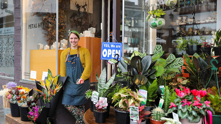 Person standing outside Petal & Fern florist surrounded by plants
