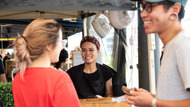 Stallholer wears headscarf and glasses as they greet two customers at Sydney Vegan Market