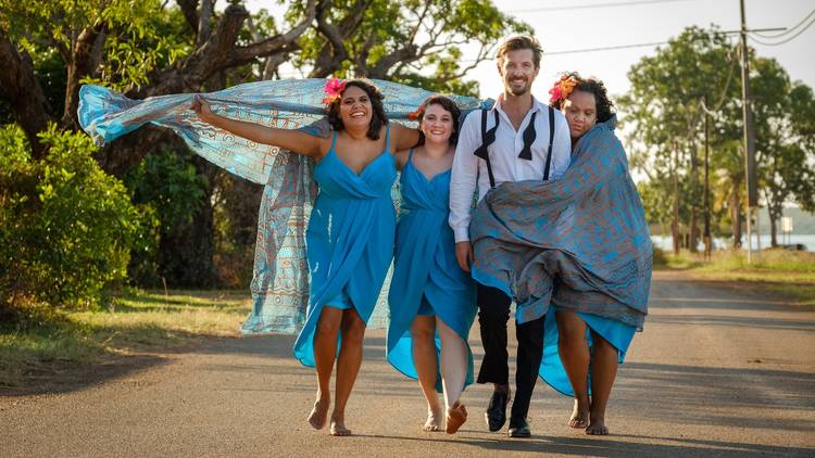 The cast of Top End Wedding walk barefoot on a road surrounded by trees
