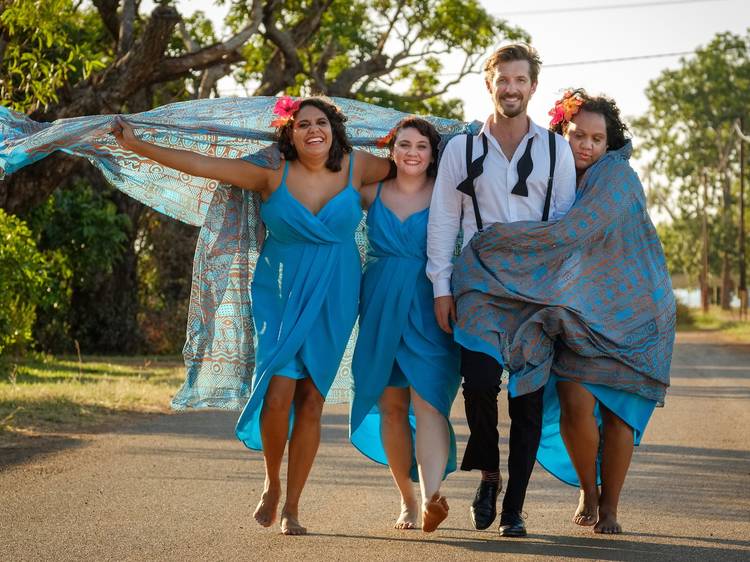 The cast of Top End Wedding walk barefoot on a road surrounded by trees