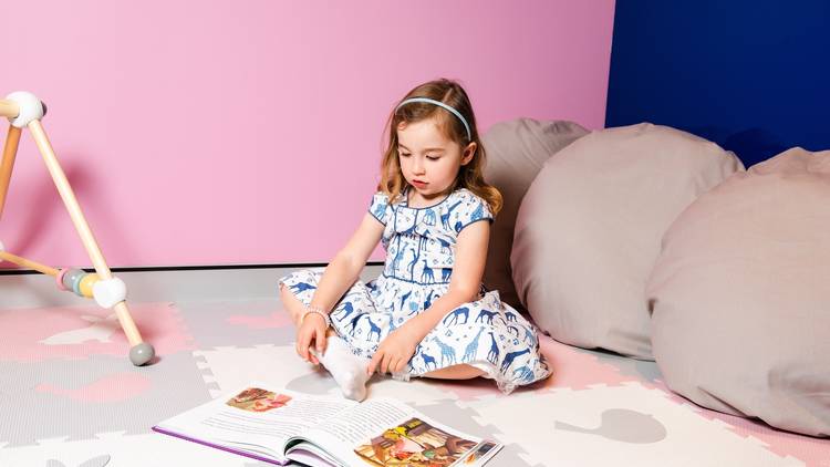 A child sits reading a book in a fun pastel environment at The Hood Créche