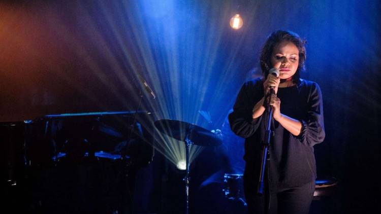 Ursula Yovich holding a microphone on a stand, backlit, about to sing