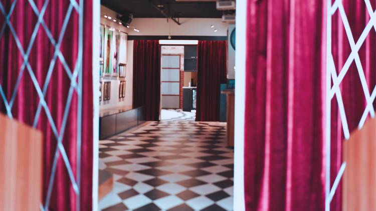 Peering through red curtains to a gallery with a checkerboard floor