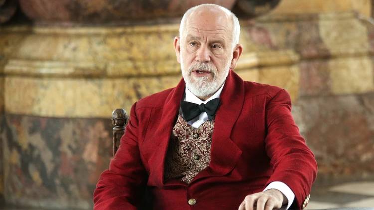 A shot of John Malkovich in a red velvet jacket, gold brocade waistcoat and black bow tie in Polish director Lech Majewski's Valley of the Gods 2020