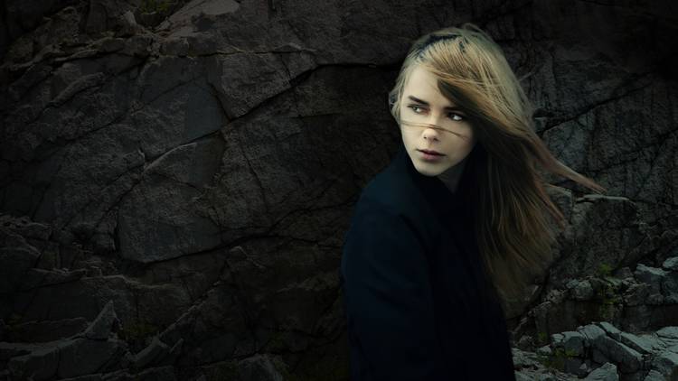 a woman with windswept hair in front of a rocky outcrop