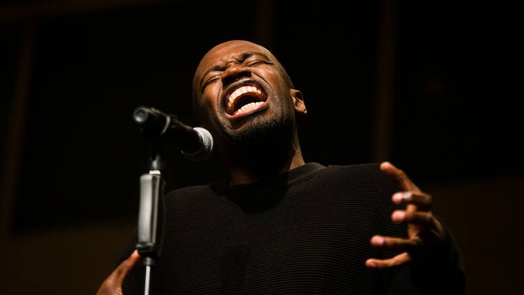 Wāni La Frère in full flow at a mic during a poetry slam performance