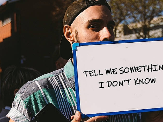 Tell Me Something I Don't Know A person wearing a tshirt and backwards-facing cap holding a whiteboard in front of their mouth that says "Tell me something I don't know"