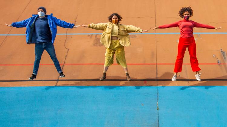 Three people doing a star jump simultaneously; each is wearing either a all blue, all red or all yellow outfit