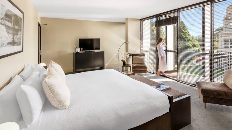 A woman in a bathrobe looking out the window in a suite at Werribee Mansion