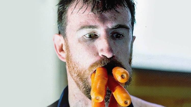 A man's face with five whole carrots sticking out of his mouth