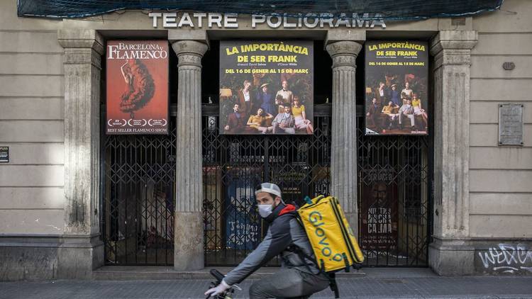 Un repartidor de Glovo passa davant del Teatre Poliorama tancat