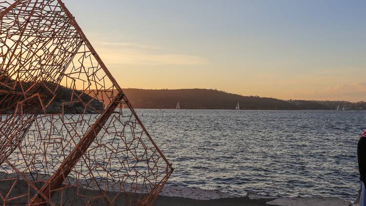 Close up of metal sculpture next to ocean view, sailboats in the distance.