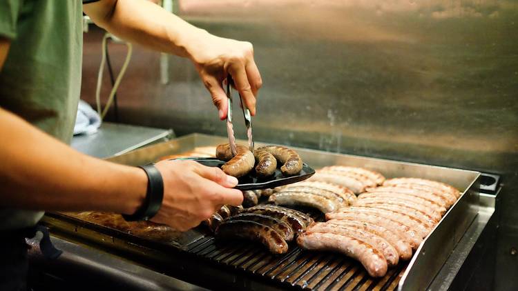 Person fills plate with sausages from industrial grill with rows of sausages.