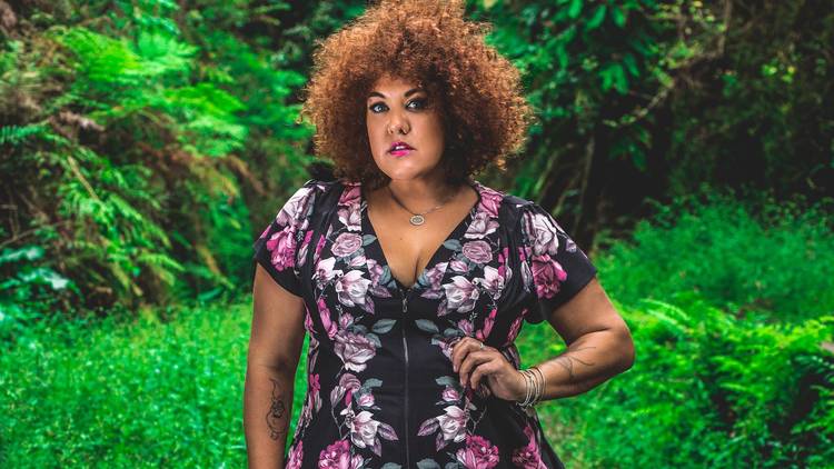 Casey Donovan poses in a purple floral dress in front of some lush greenery