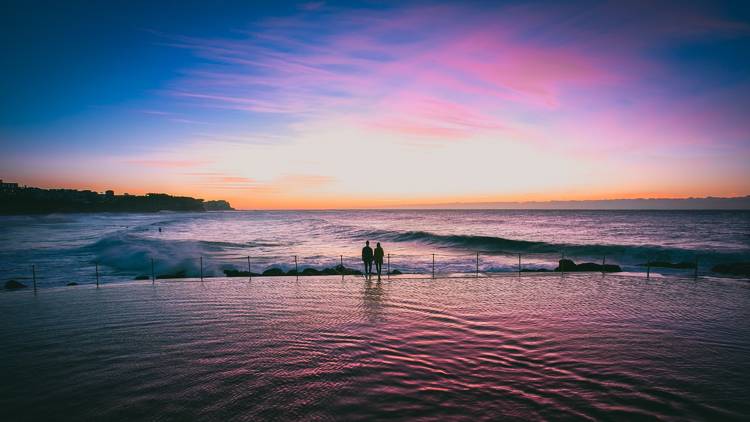 Two people silhouetted at Bronte pool at sunset