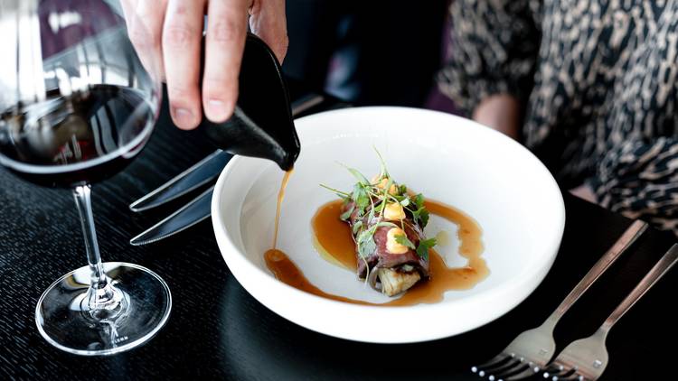 A fancy restaurant dish with the sauce being added by a waiter