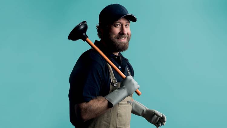 A man in overalls cap and short shirt with hairy arms holds a toilet plunger aloft