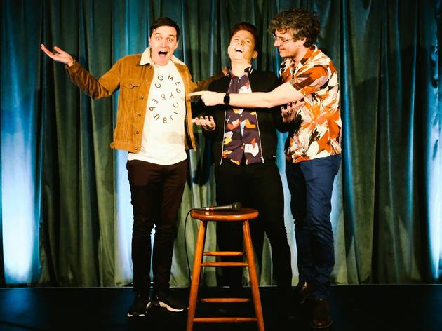 Comedy Republic Alex Dyson, Rhys Nicholson and Kyran Whealey smiling and laughing around a wooden stool, on a stage