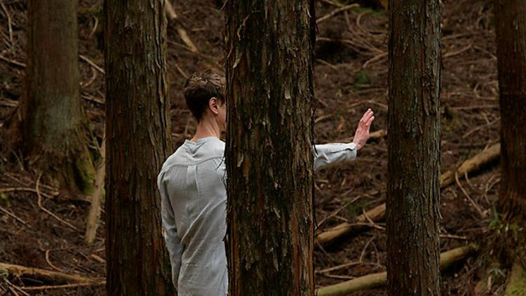 A man person with short hair stands in a forest with their arm and palm outstretched