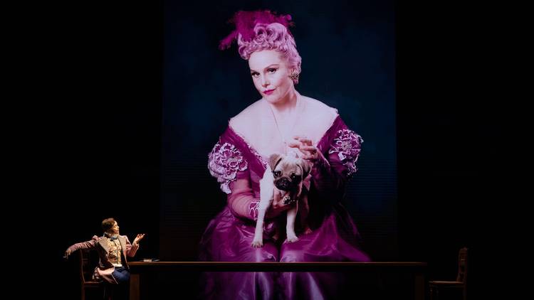 Eryn Jean Norvial in pink ress holding apug, and in a suit, looking up at the big screen image of herself in another roleSydney Theatre Company 2020