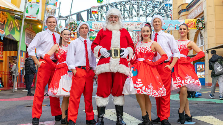 Santa and bunch of white and red clad people stand in front of Luna Park