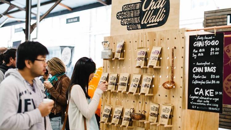 People browse market stalls with chai teas and gifts.