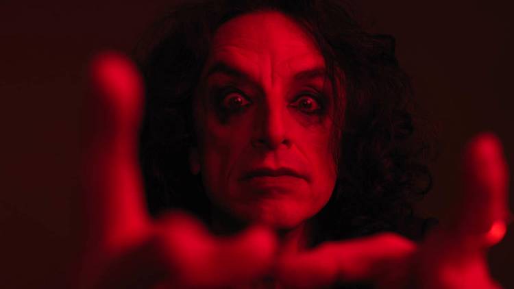A close-up of Paul Capsis with dark eye makeup, bathed in red light