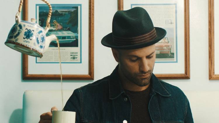 Magician James galea in a denim jacket and hat with a floating kettle filling his tea cup