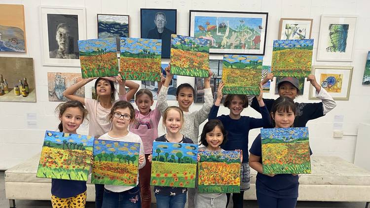 Group of children hold up paintings in a gallery